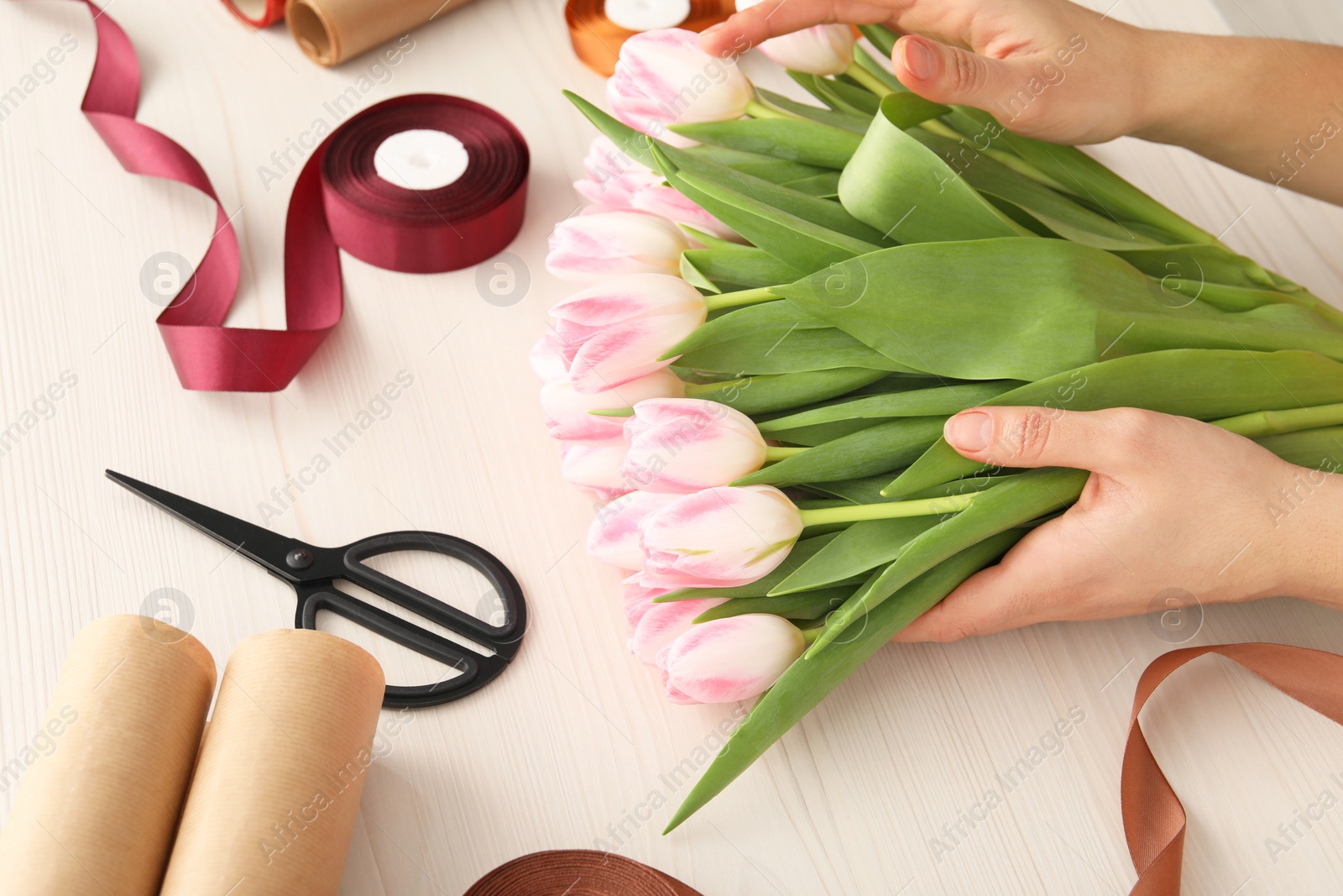 Photo of Woman making bouquet of beautiful fresh tulips at white wooden table, closeup