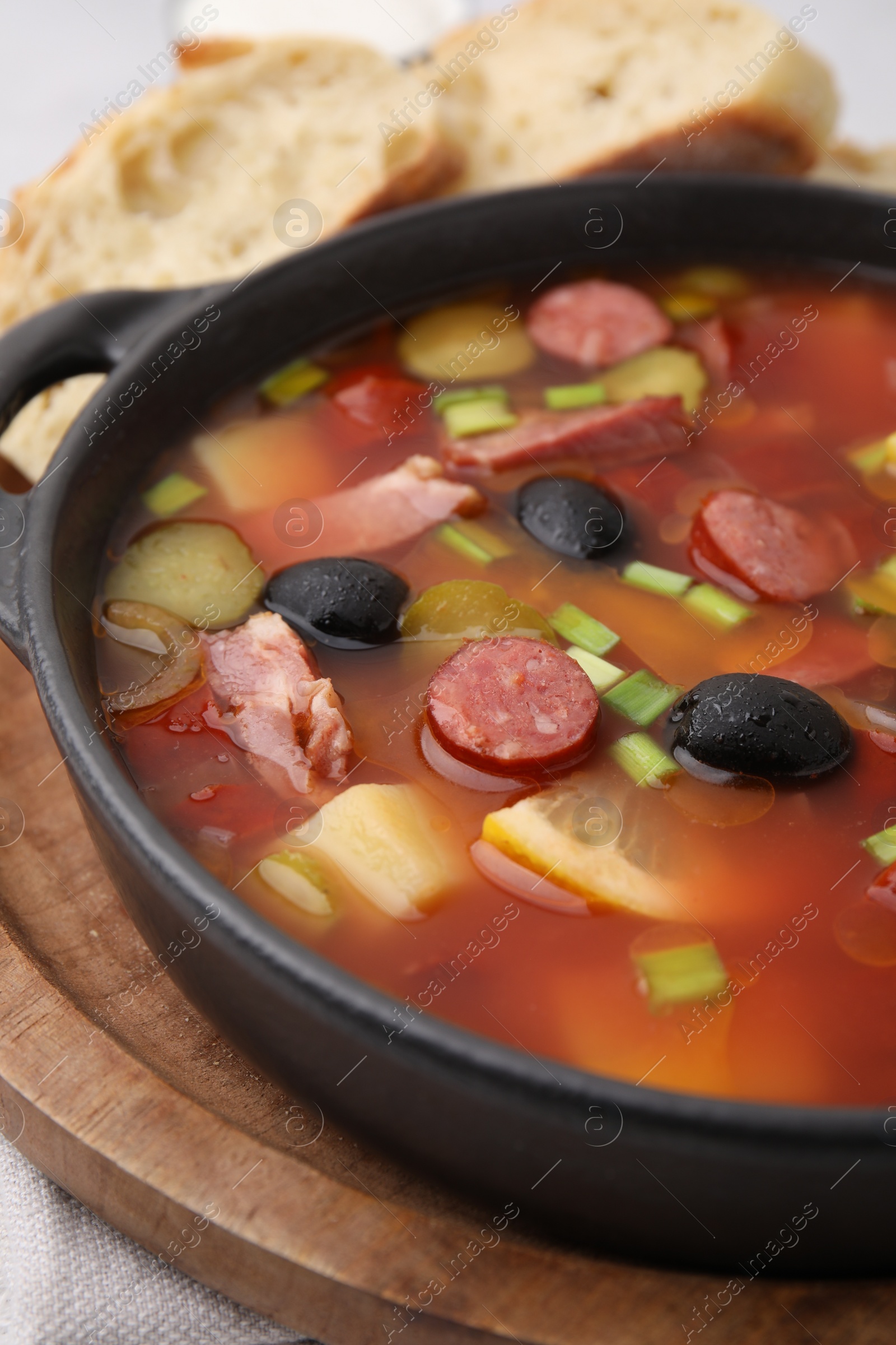 Photo of Meat solyanka soup with thin dry smoked sausages in bowl on table, closeup