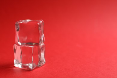 Photo of Crystal clear ice cubes on red background, closeup. Space for text