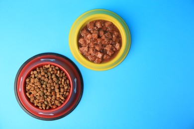 Photo of Wet and dry pet food in feeding bowls on light blue background, flat lay. Space for text