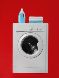 Modern washing machine with stack of towels and detergent on red background. Laundry day