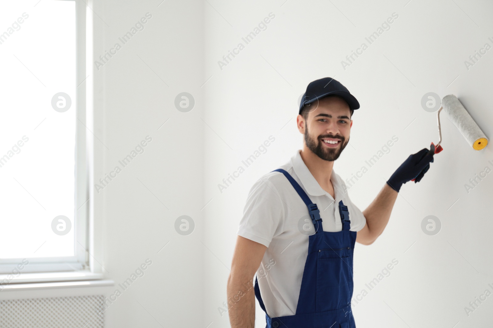 Photo of Handyman painting wall with roller brush indoors, space for text. Professional construction tools