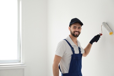 Handyman painting wall with roller brush indoors, space for text. Professional construction tools