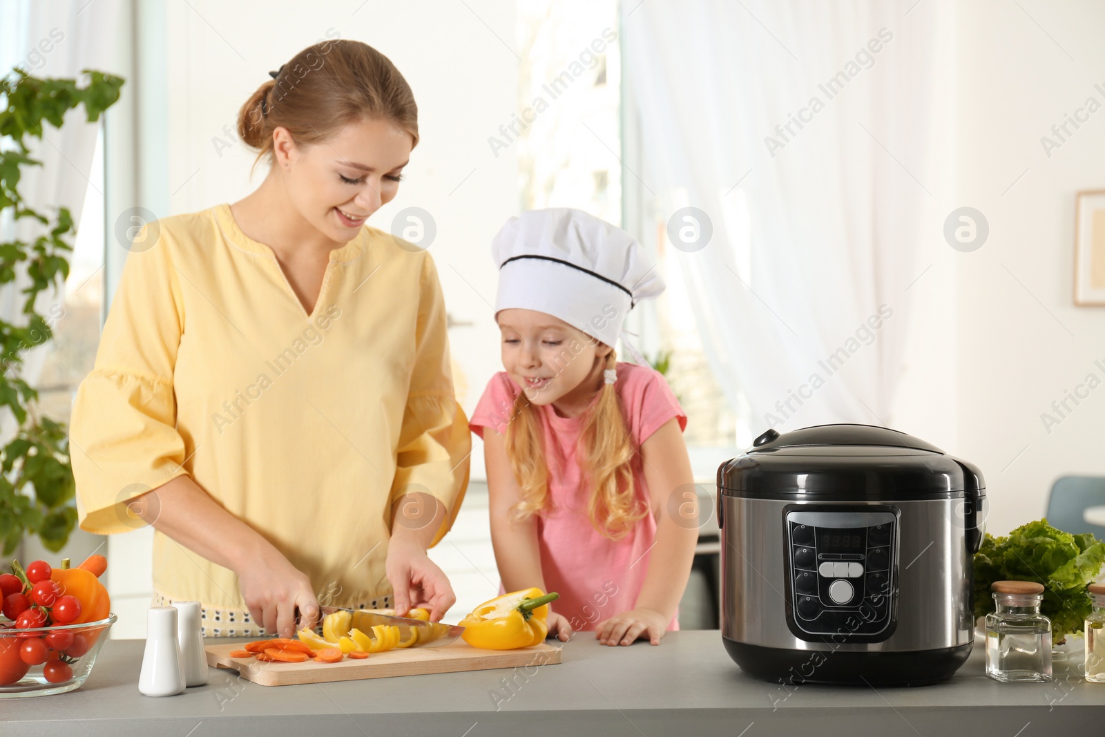 Photo of Mother and daughter preparing food with modern multi cooker in kitchen