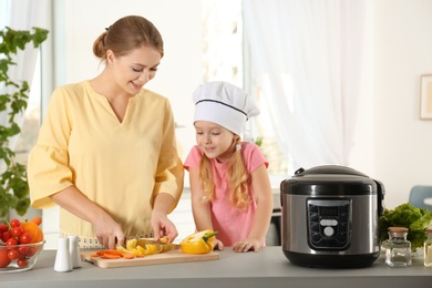 Mother and daughter preparing food with modern multi cooker in kitchen