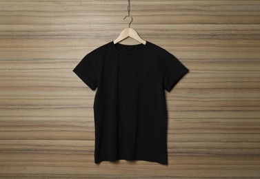 Photo of Hanger with stylish black T-shirt on wooden wall