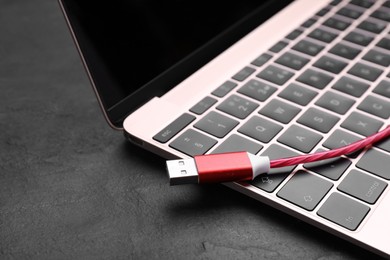 Photo of Red USB cable and laptop on black slate table, closeup