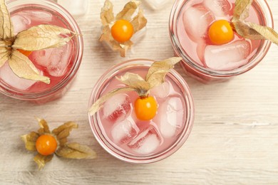 Photo of Refreshing cocktail decorated with physalis fruits on wooden table, flat lay