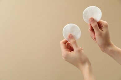 Photo of Woman holding cotton pads on beige background, closeup. Space for text