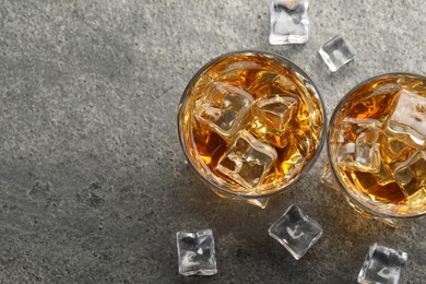 Whiskey and ice cubes in glasses on grey textured table, top view. Space for text