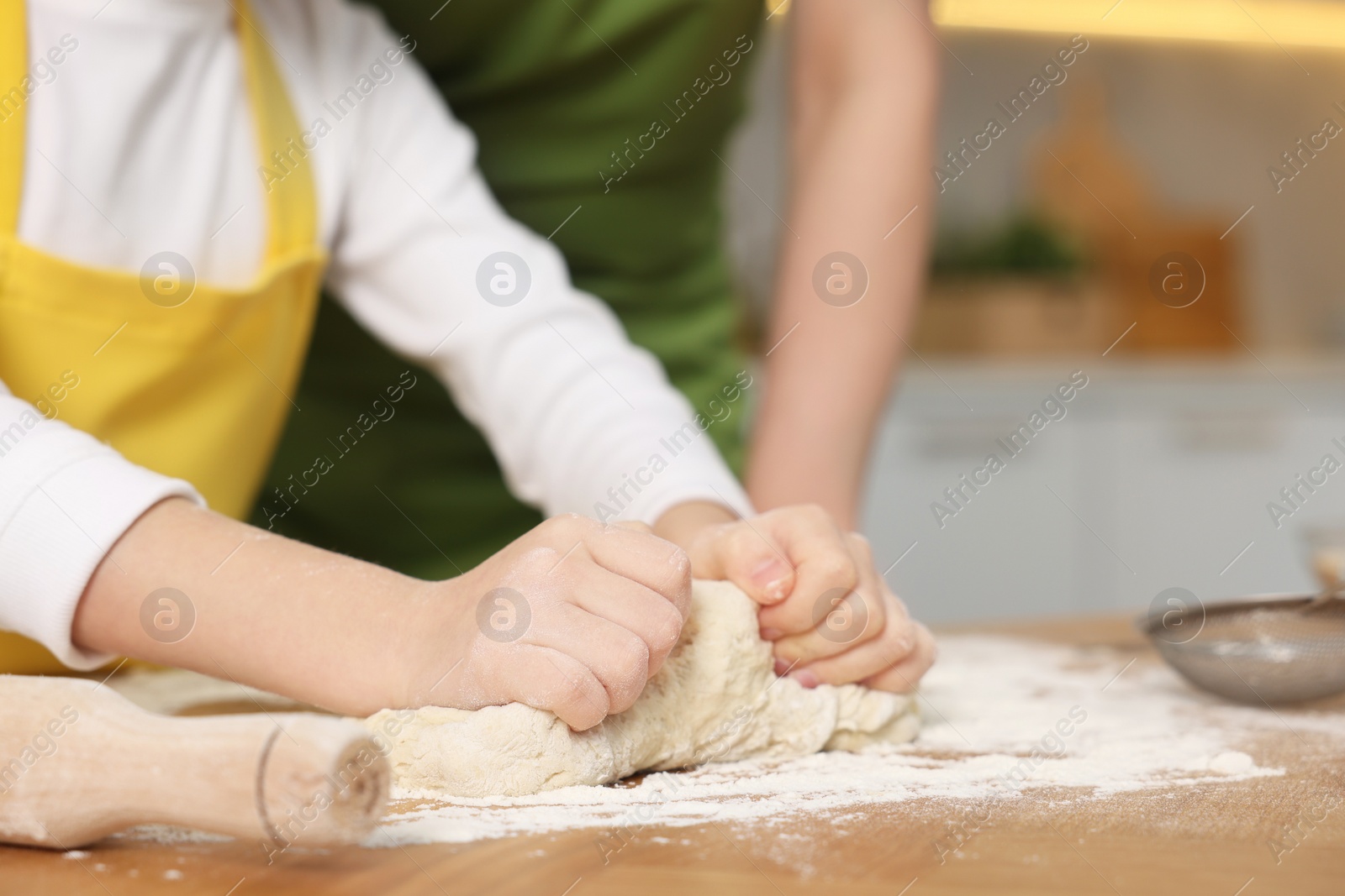 Photo of Making bread. Mother and her daughter kneading dough at wooden table in kitchen, closeup