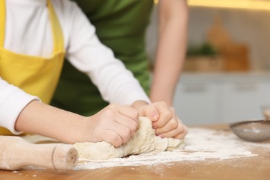 Making bread. Mother and her daughter kneading dough at wooden table in kitchen, closeup