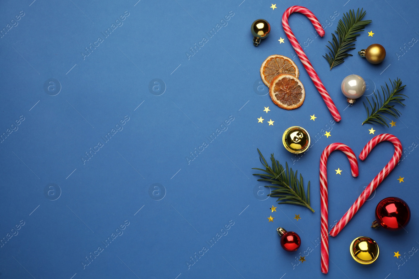 Photo of Flat lay composition with sweet candy canes and Christmas decor on blue background, space for text