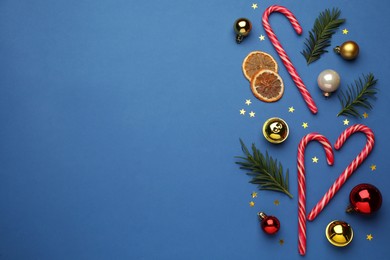 Flat lay composition with sweet candy canes and Christmas decor on blue background, space for text