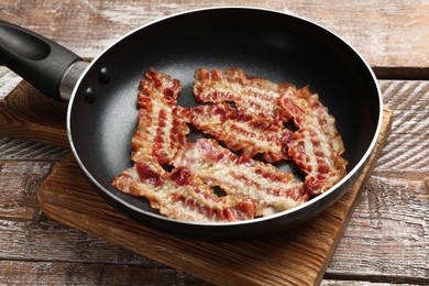 Delicious bacon slices in frying pan on wooden table, closeup