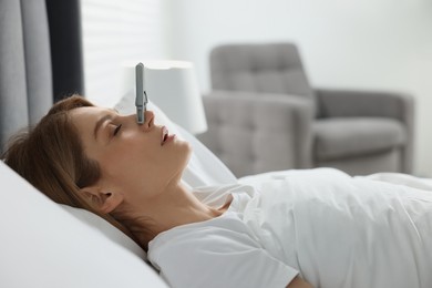 Photo of Woman sleeping with clothespin on her nose in bed at home. Problem with snoring