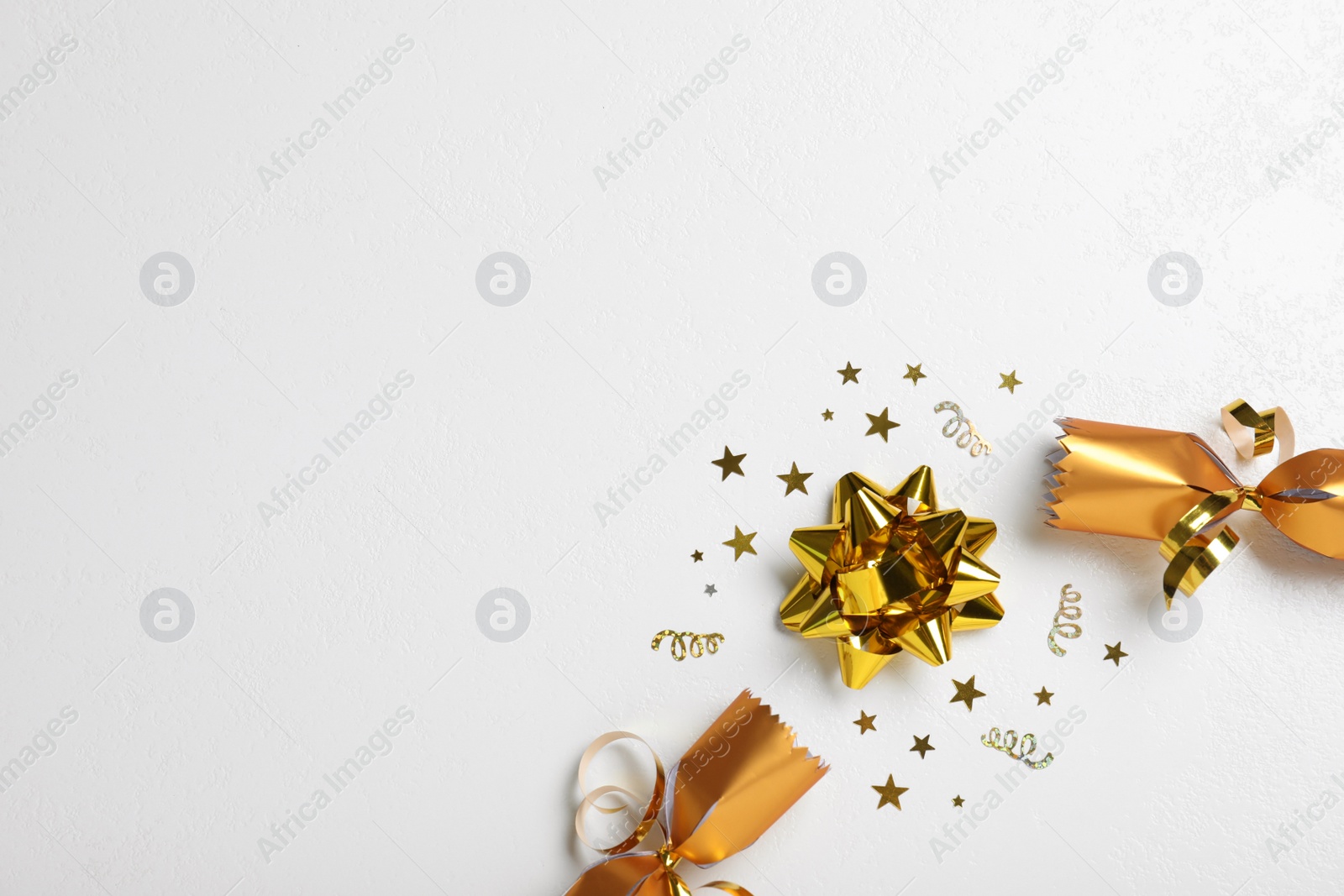 Photo of Open golden Christmas cracker with bow and shiny confetti on white background, flat lay. Space for text