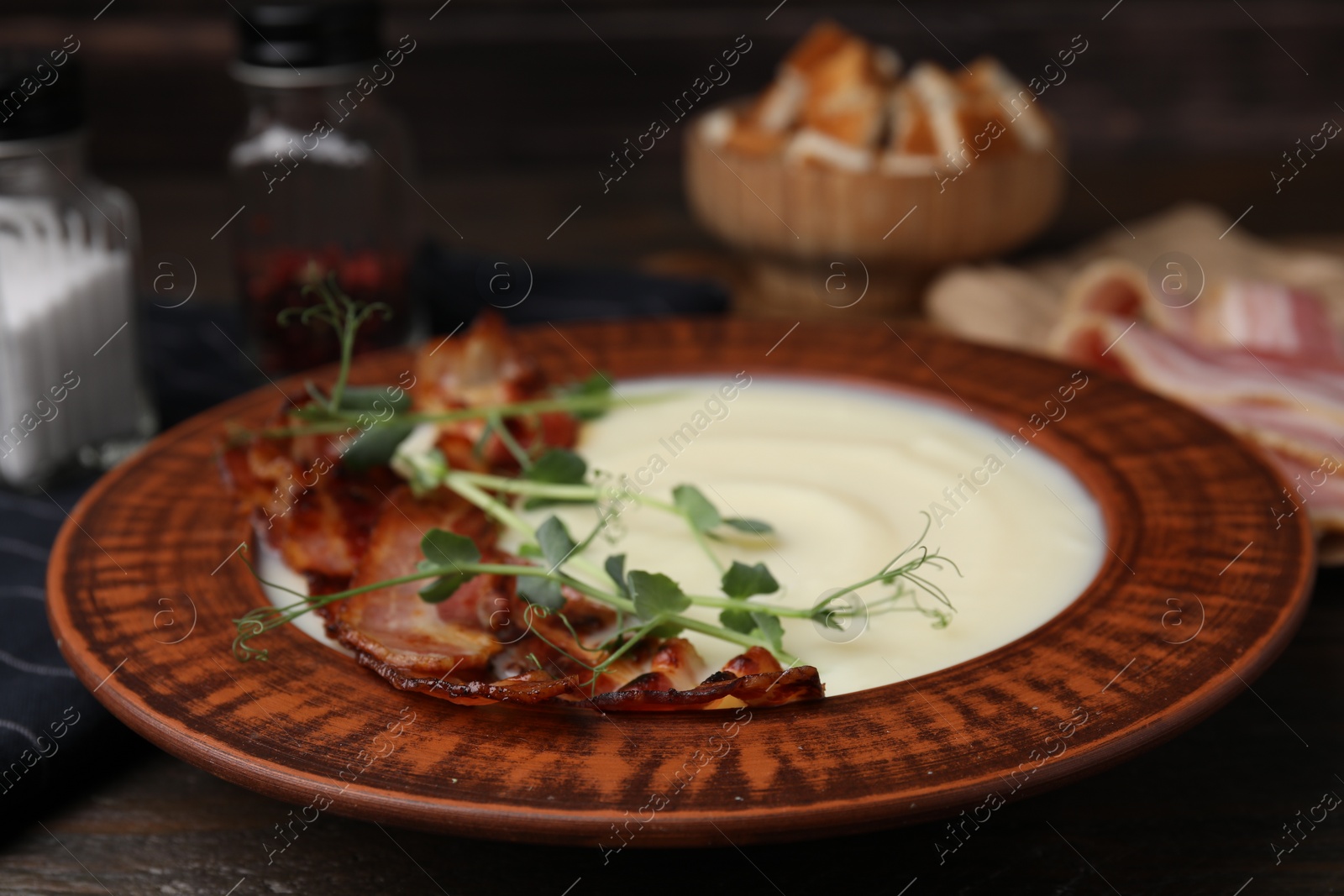 Photo of Delicious potato soup with bacon and microgreens in bowl on table, closeup