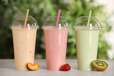 Photo of Plastic cups with different tasty smoothies and fresh fruits on wooden table outdoors