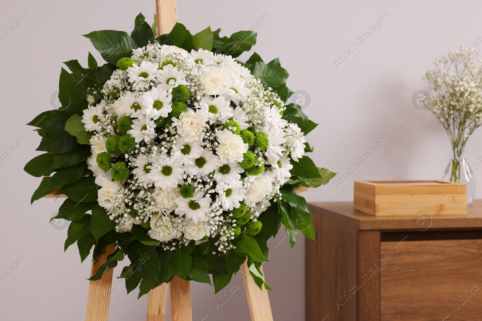 Photo of Funeral wreath of flowers on wooden stand near grey wall in room