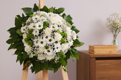 Funeral wreath of flowers on wooden stand near grey wall in room