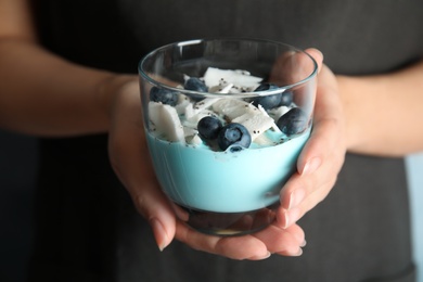 Woman holding glass cup of spirulina smoothie with blueberries, coconut and chia seeds, closeup