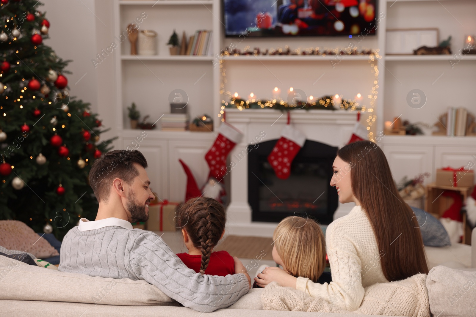 Photo of Happy family spending time on sofa near TV in cosy room, back view. Christmas atmosphere