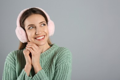 Photo of Happy woman wearing warm earmuffs on grey background, space for text
