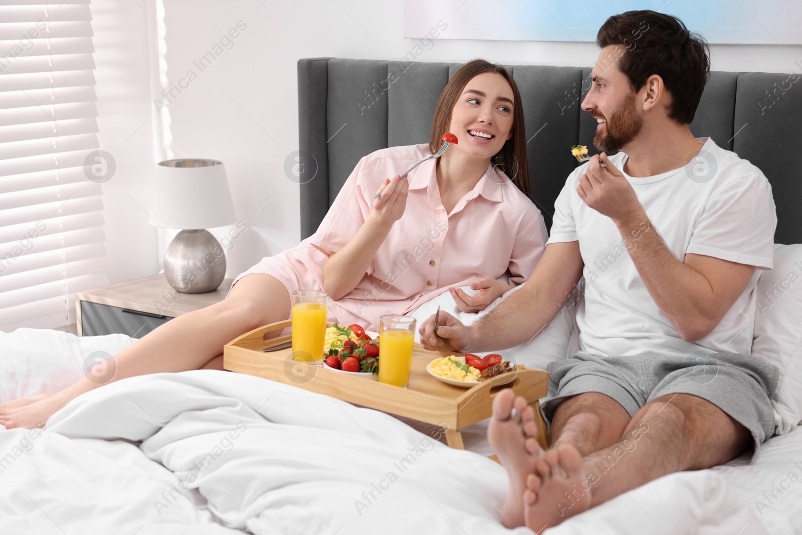 Photo of Happy couple having breakfast and talking on bed at home