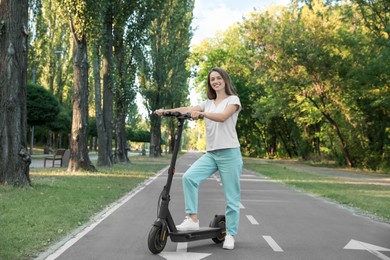 Happy woman with modern electric kick scooter in park