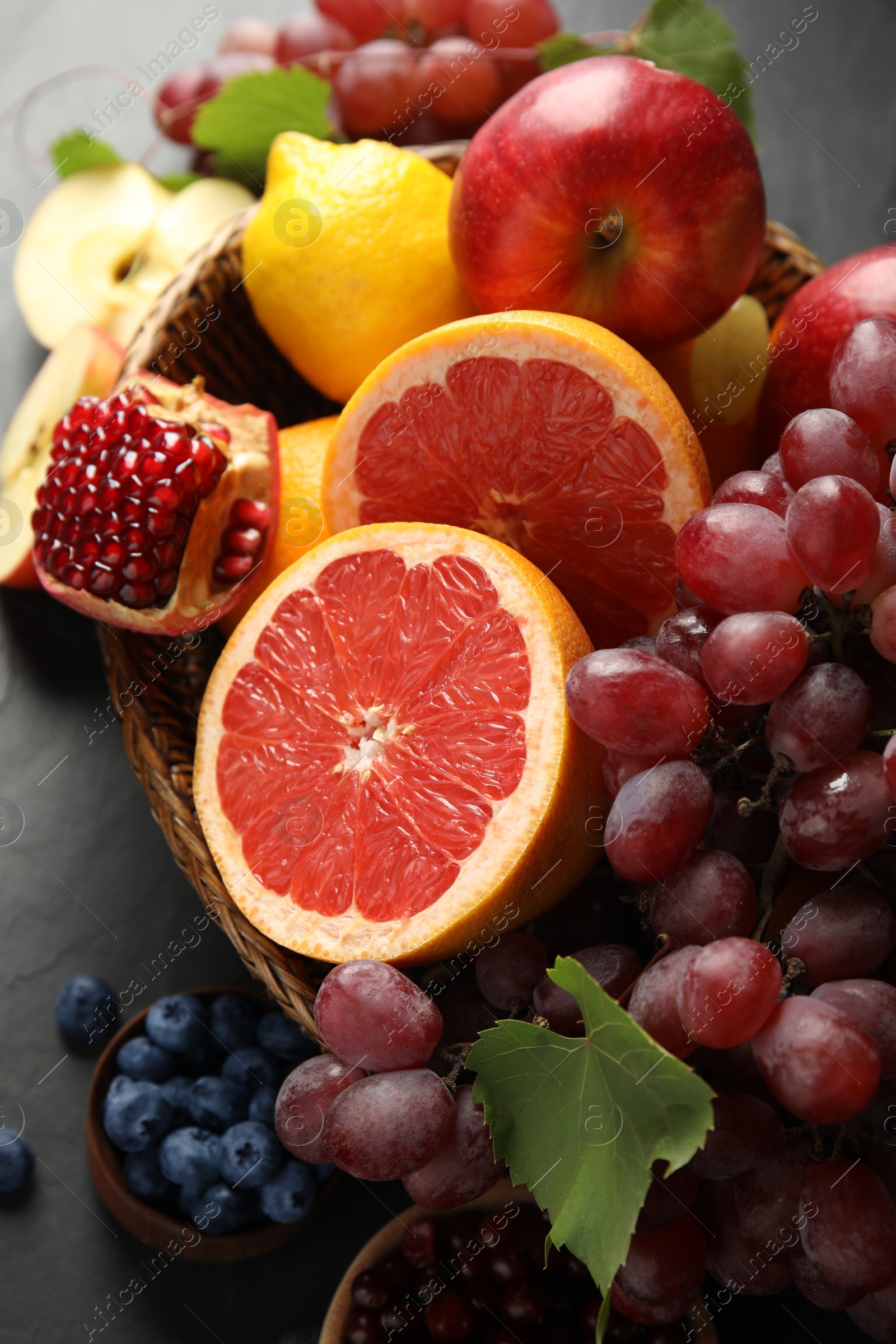 Photo of Wicker basket with different fruits berries on black table, closeup