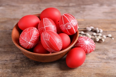 Photo of Wooden bowl with red painted Easter eggs on table