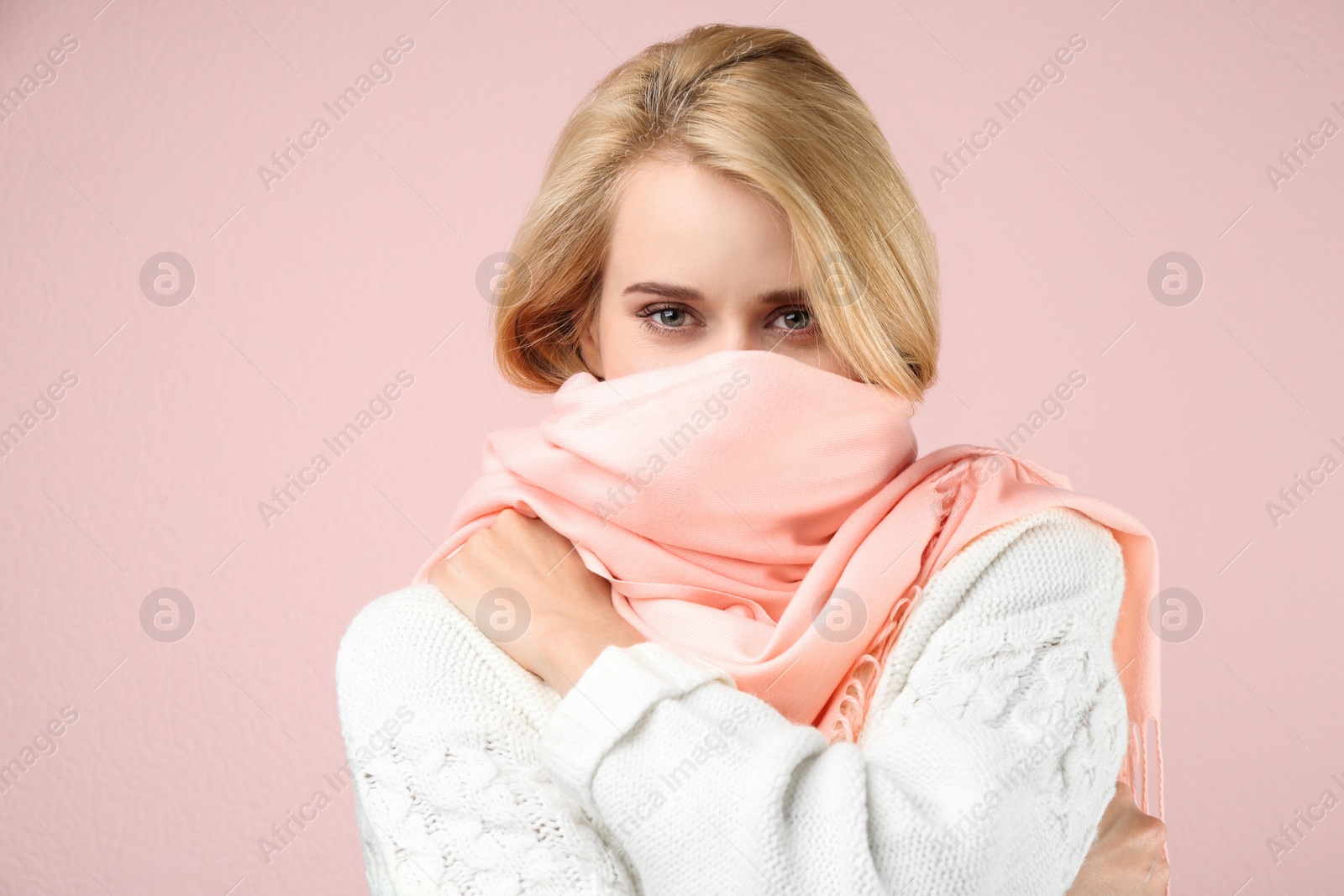 Photo of Beautiful woman wearing warm scarf on pink background. Autumn clothes