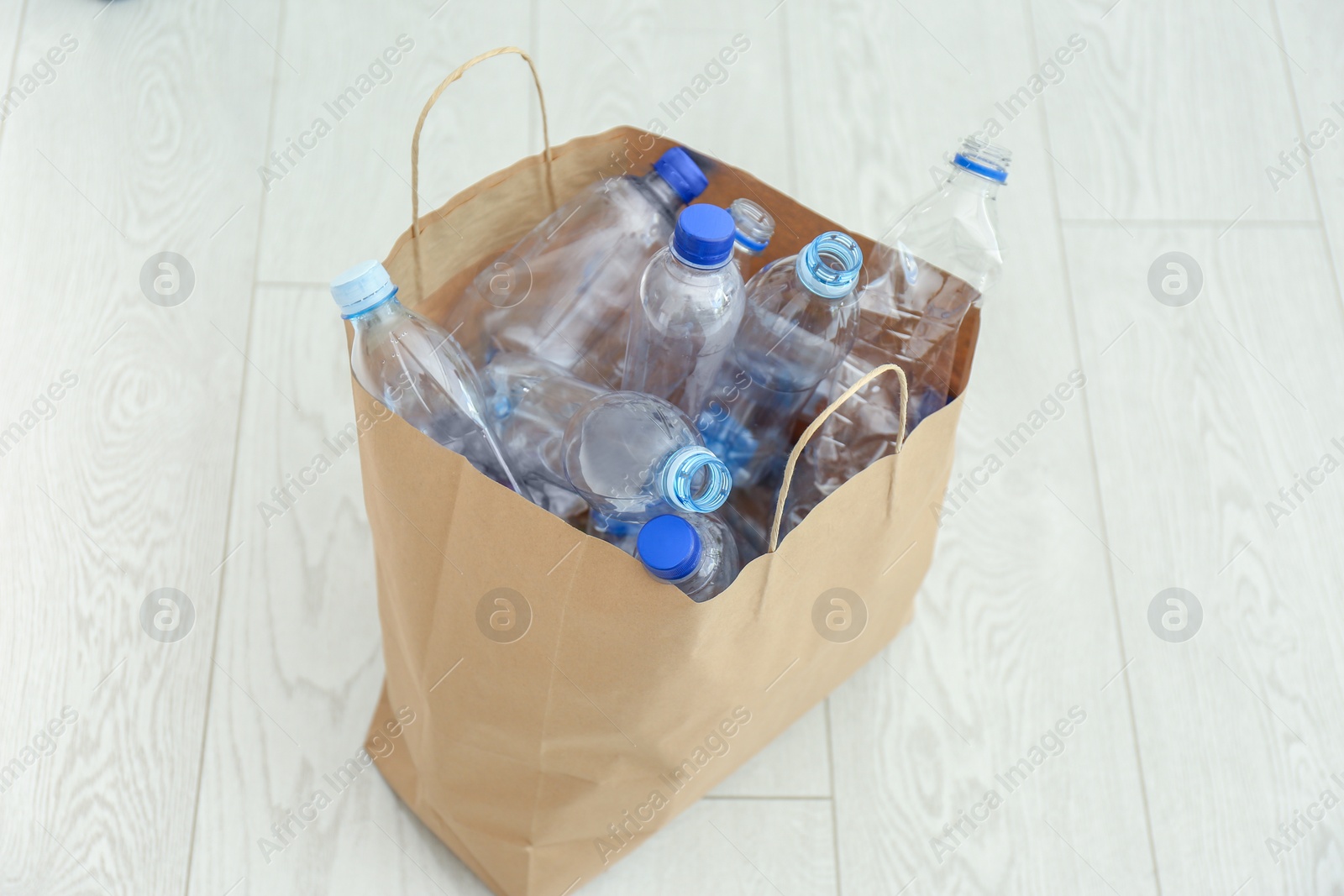 Photo of Paper bag with used plastic bottles on floor. Recycle concept