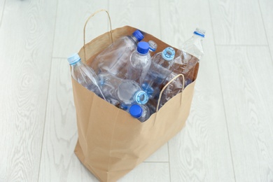 Photo of Paper bag with used plastic bottles on floor. Recycle concept