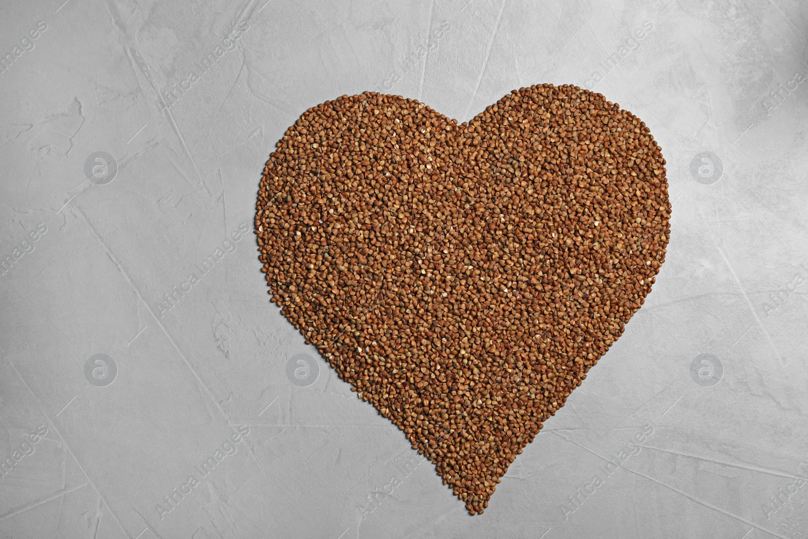 Photo of Heart made of raw buckwheat on grey background, top view. Space for text