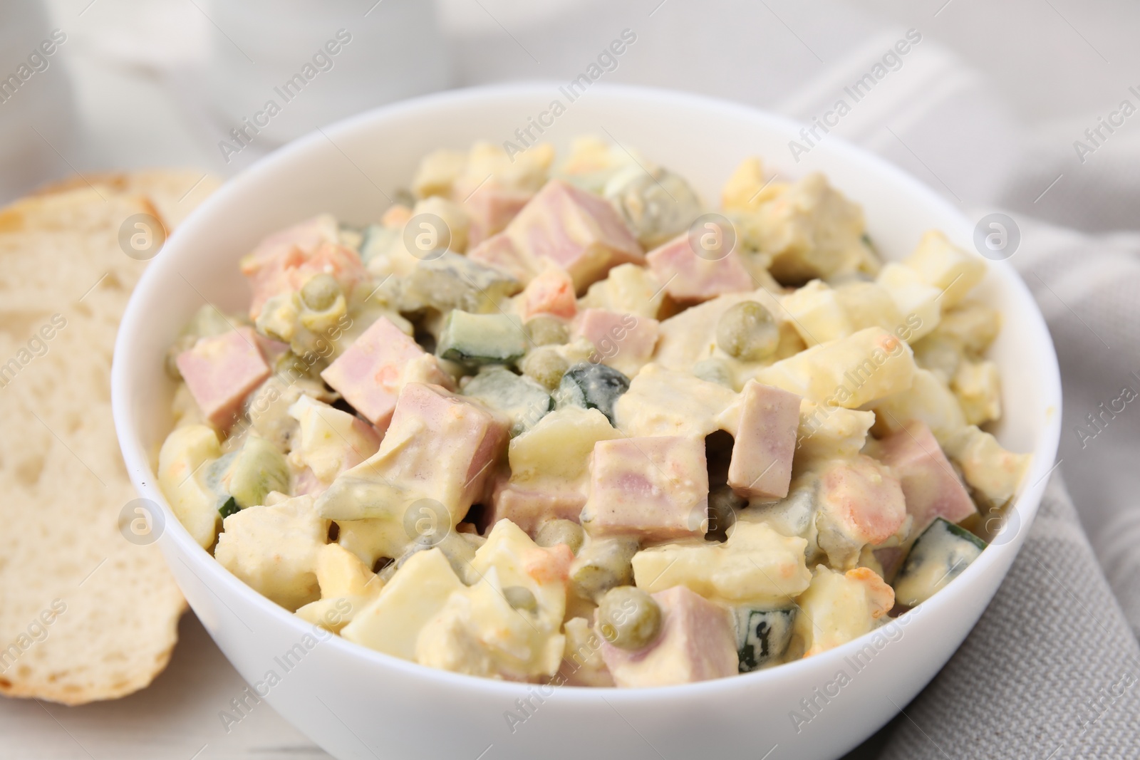 Photo of Tasty Olivier salad with boiled sausage in bowl on white table, closeup