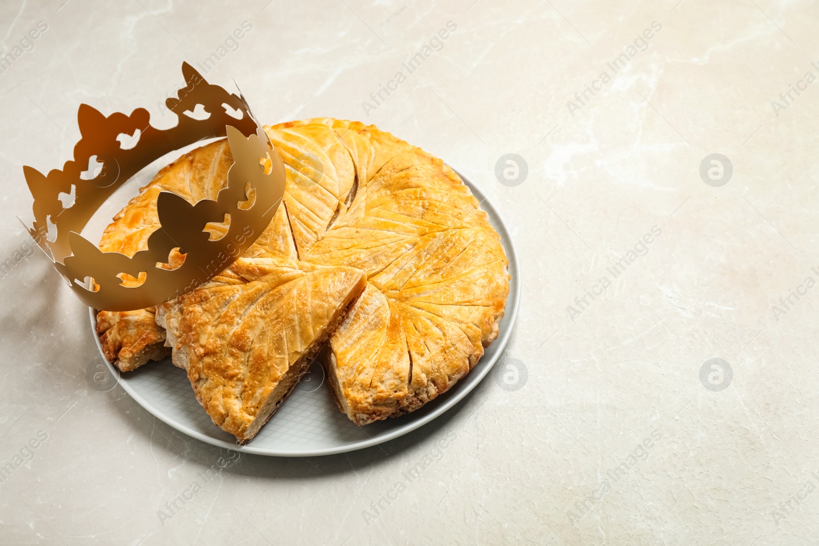 Photo of Traditional galette des Rois with paper crown on light grey marble table. Space for text