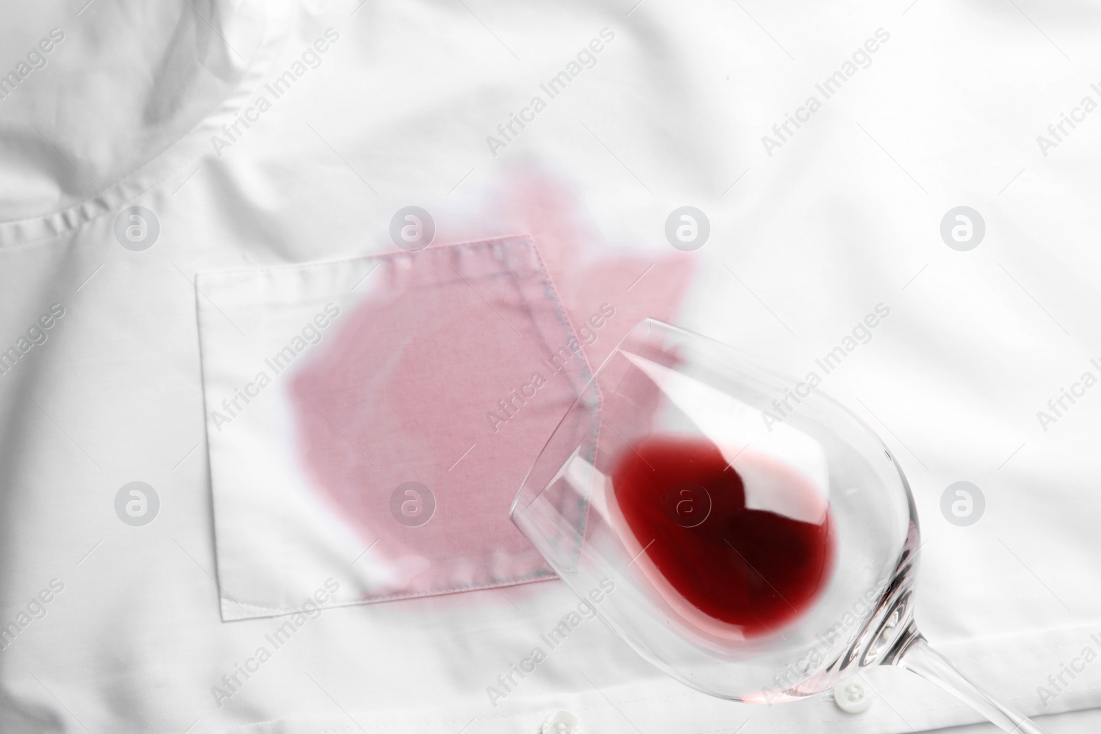 Photo of Overturned glass and spilled exquisite red wine on white shirt, top view. Space for text