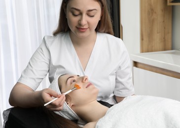 Photo of Cosmetologist with brush applying cosmetic product to client`s face in clinic