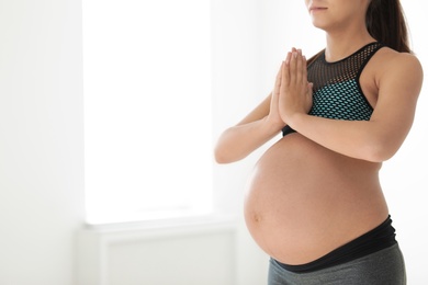 Young pregnant woman in fitness clothes practicing yoga at home, closeup. Space for text