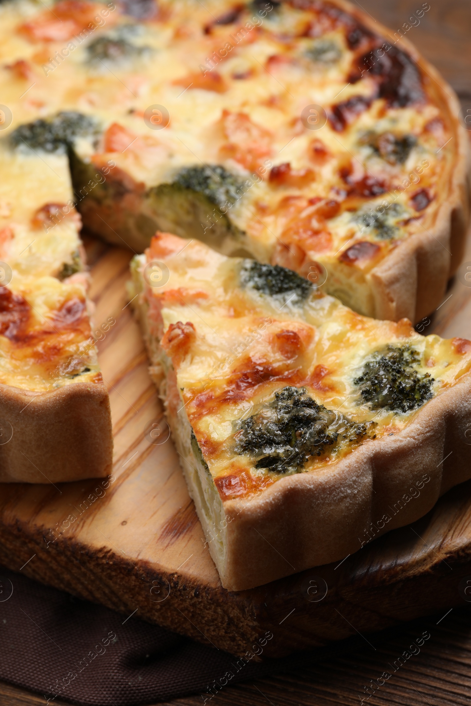 Photo of Delicious homemade quiche with salmon and broccoli on wooden board, closeup