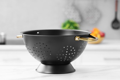 Photo of Black colander on white marble table in kitchen, closeup