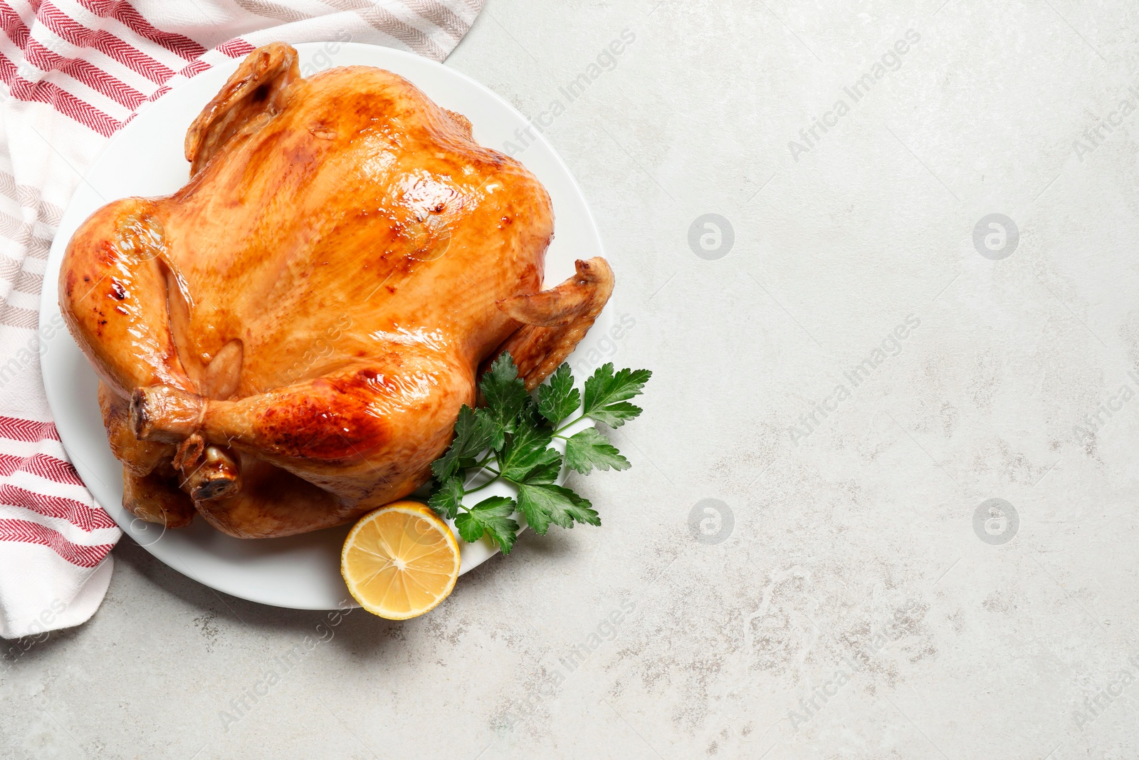 Photo of Tasty roasted chicken with parsley and lemon on light grey table, top view. Space for text