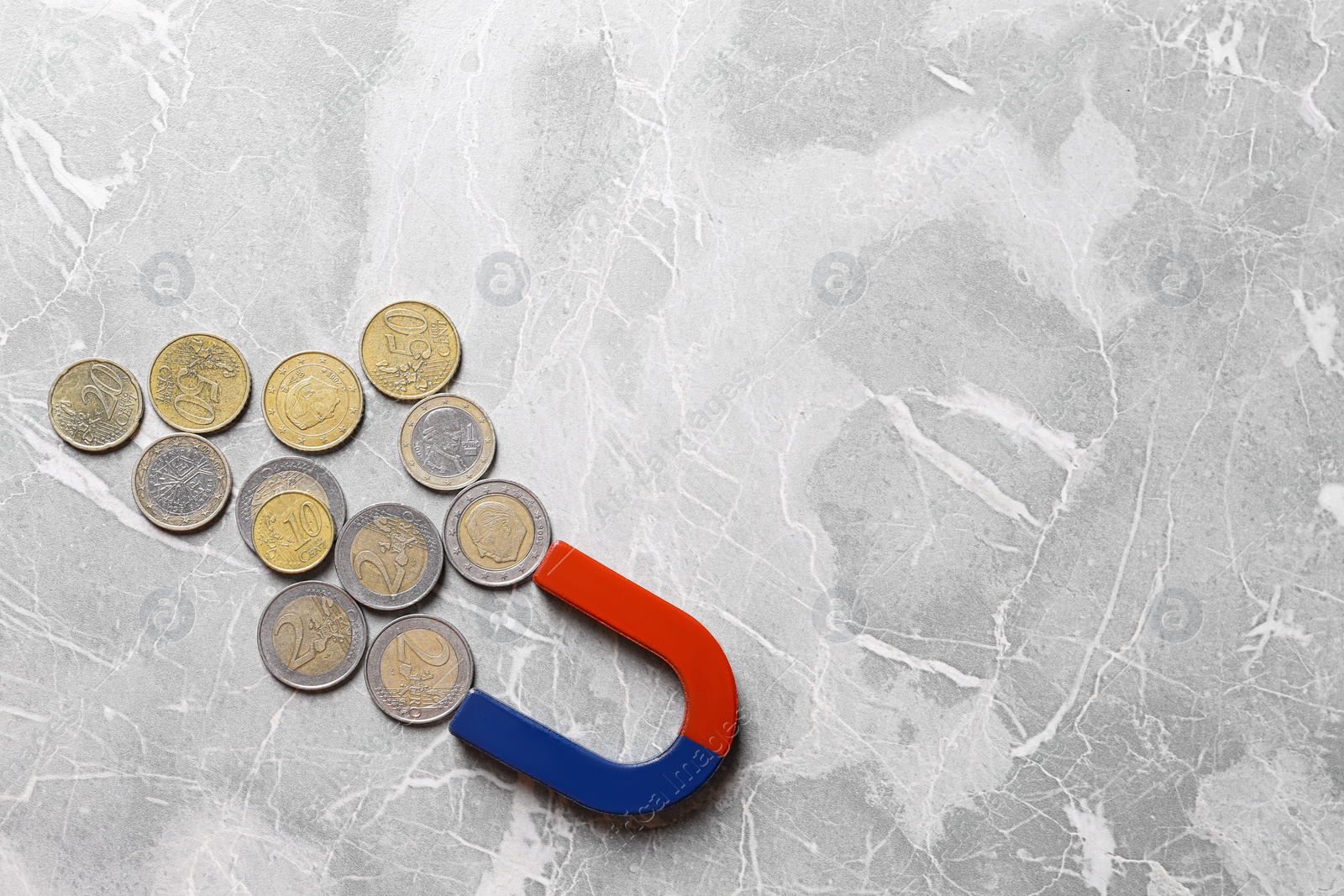 Photo of Red and blue horseshoe magnet attracting coins on grey marble background, flat lay. Space for text