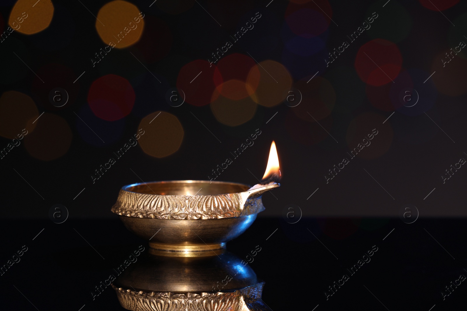 Photo of Lit diya on dark background with blurred lights, space for text. Diwali lamp