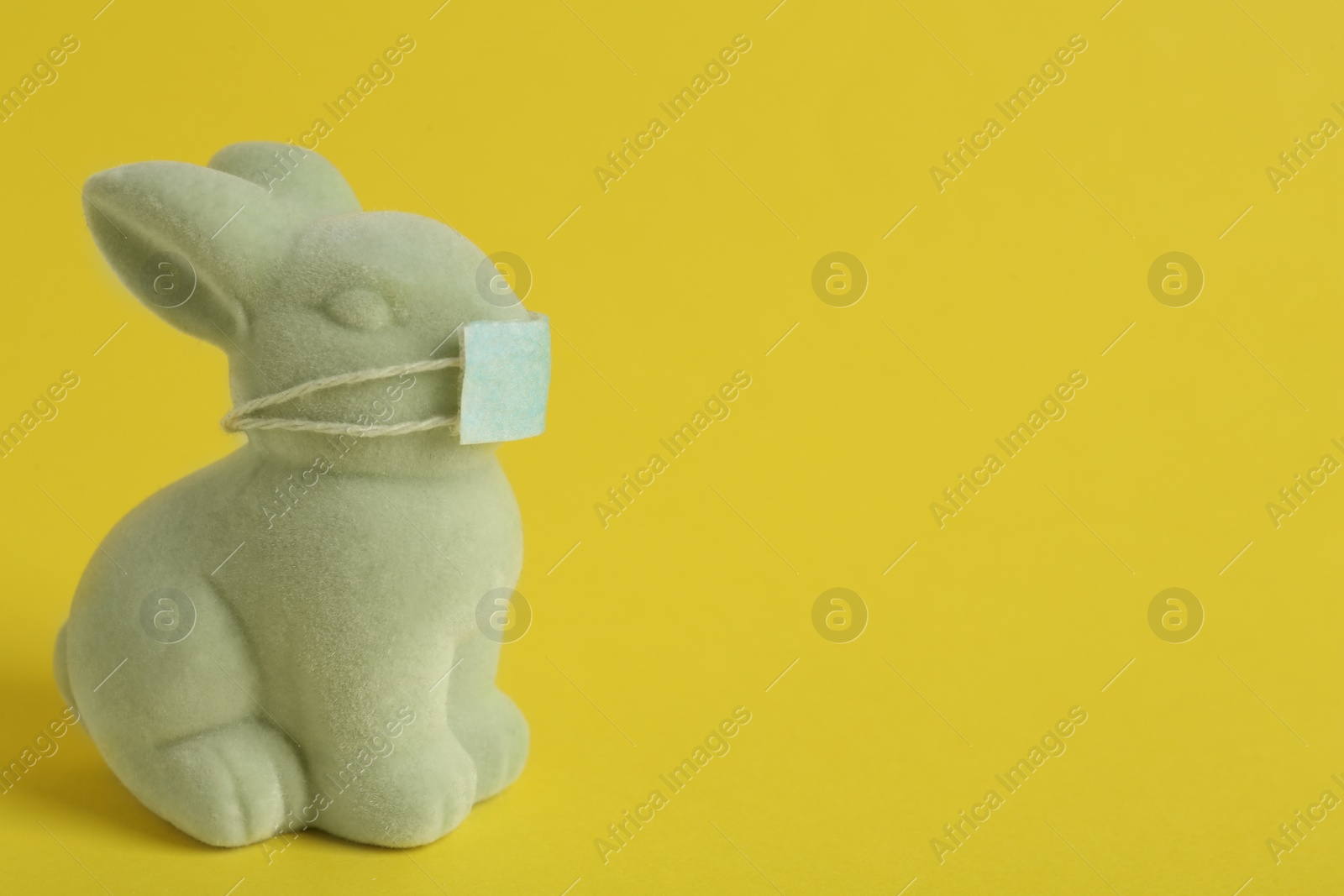 Photo of Cute bunny figure in protective mask on yellow background, space for text. Easter holiday during COVID-19 quarantine