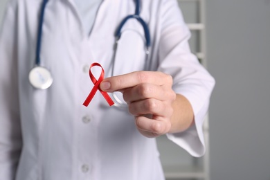Doctor holding red awareness ribbon indoors, closeup. World AIDS disease day