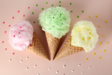 Photo of Sweet cotton candies in waffle cones on beige background, flat lay