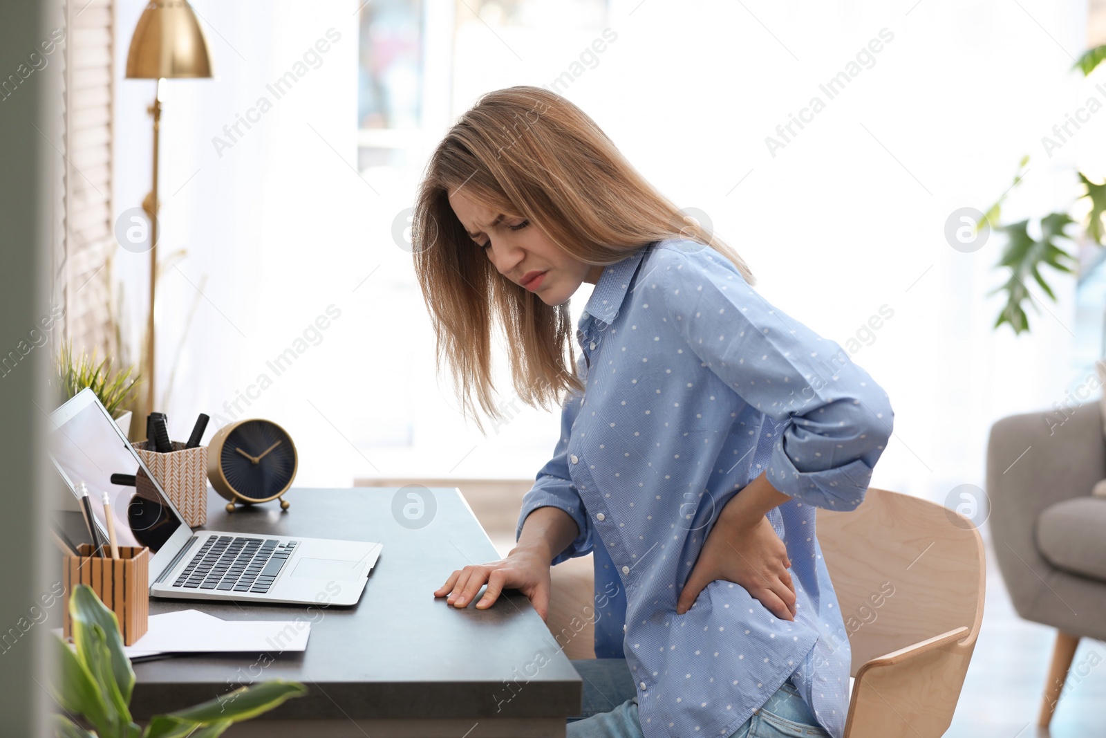 Photo of Young woman suffering from back pain in office